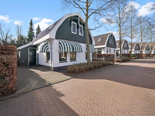 A row of modern, two-story houses with a distinctive curved roof design, arranged in a residential area with a paved driveway and well-maintained hedges.