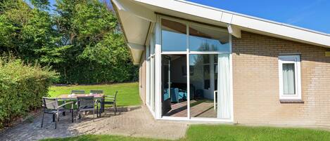 A modern house with a glass door leading to a patio with outdoor furniture.