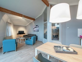 A modern living room with a sofa, a TV, and a dining table with a tray of glasses and plates.