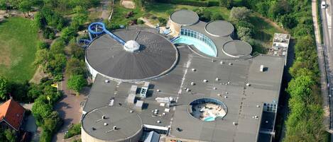 An aerial view of a building with multiple cylindrical structures, a large circular dome, and a parking area.
