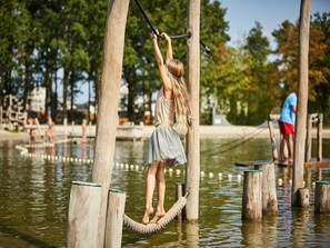 A person on a rope bridge over water, surrounded by wooden posts and trees. - Villa With Sauna & Bubble Bath in Limburg (Roggel)