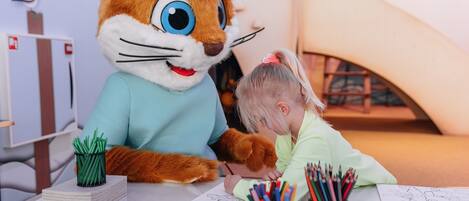 A child drawing with a large, colorful mascot at a table with art supplies.