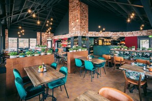En restaurang med träbord och stolar, tegelväggar och hängande lampor.