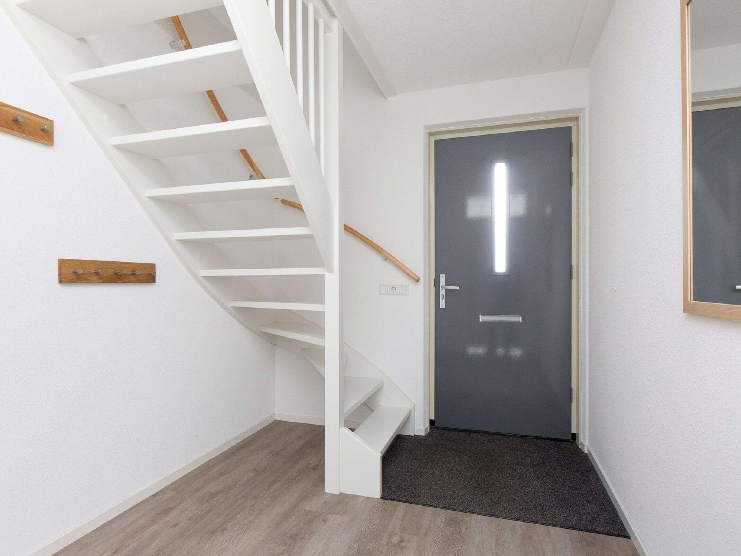 A modern interior with a white staircase, a dark door, and a wooden coat rack.