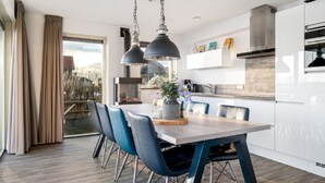 Une cuisine moderne avec des meubles blancs, un coin repas doté d’une table en bois et de chaises bleues, et une grande fenêtre agrémentée de rideaux.