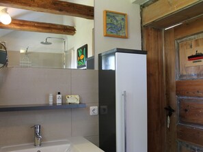 A bathroom with a white sink, a mirror, a shower, a wooden door, and a small shelf with toiletries. - Ferienwohnung in Steffenshagen mit Garten (Steffenshagen)