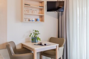 Ein modernes Zimmer mit Holztisch, zwei Stühlen, einem Blumentopf, einem flachbildfernseher an der Wand und einem fenster mit Vorhängen.