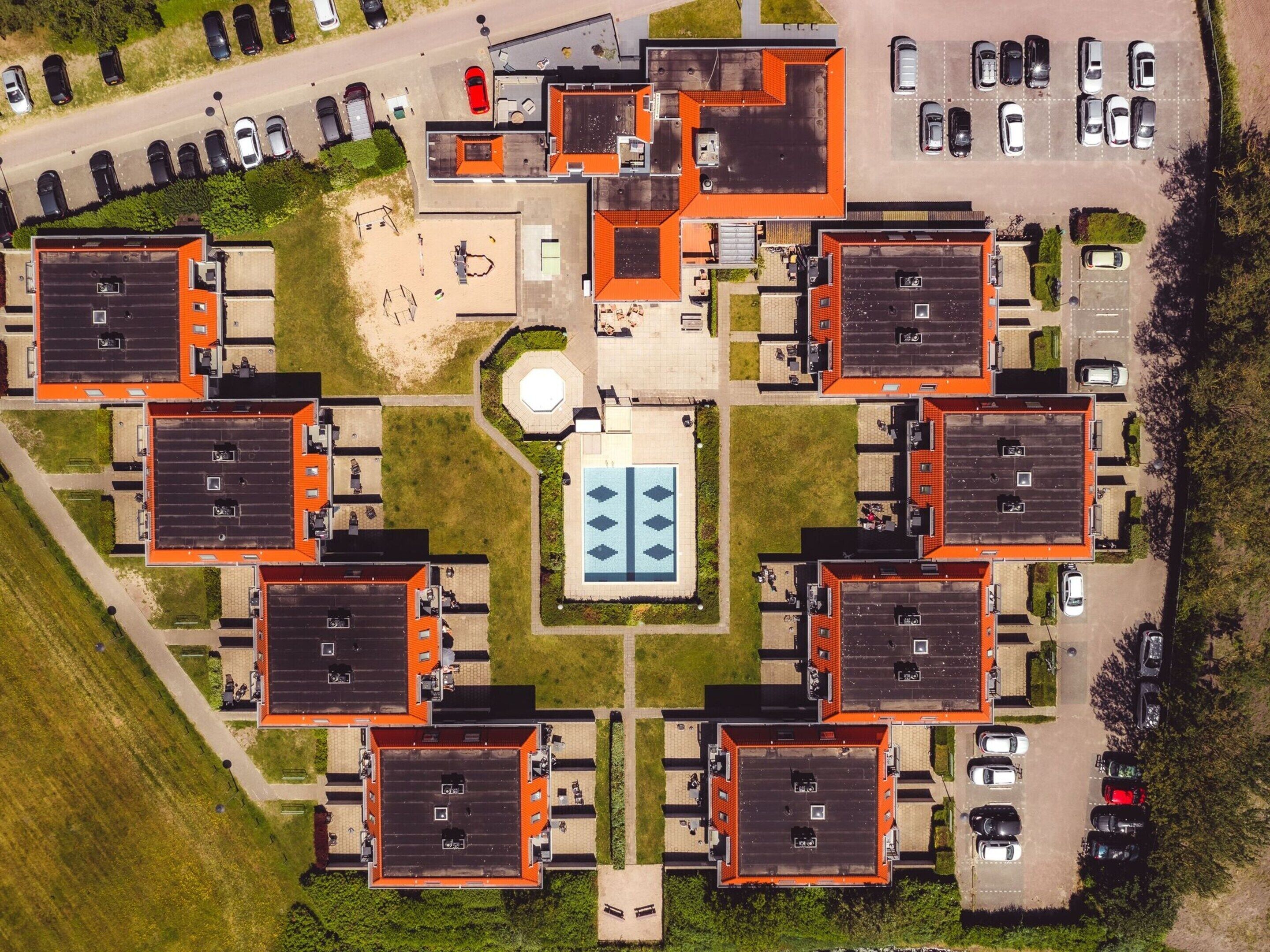Vista aérea de un complejo residencial con varios edificios de apartamentos, un patio central y un área de estacionamiento.