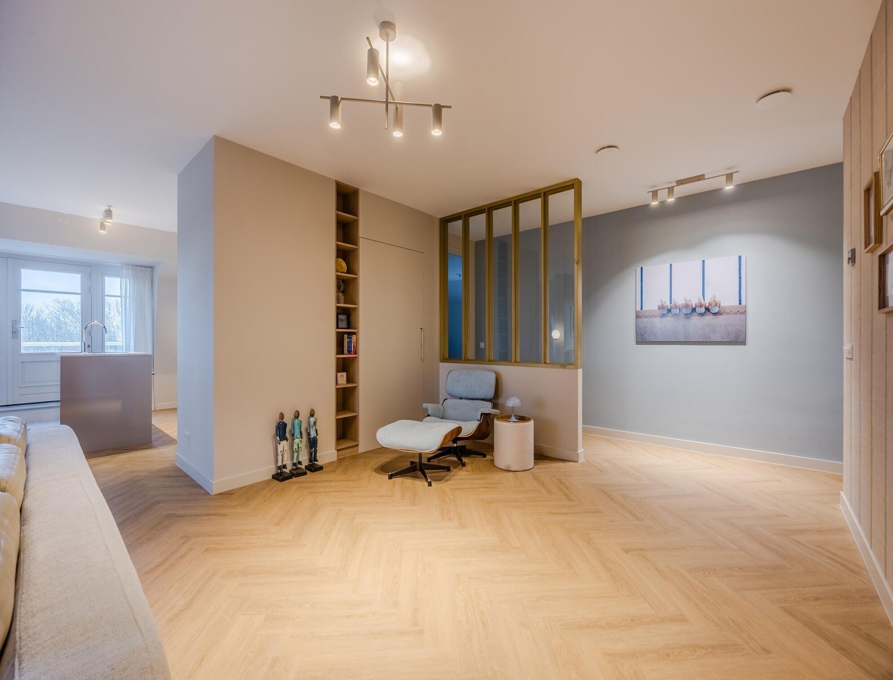 Ein modernes, helles Zimmer mit Holzboden, integriertem Kleiderschrank, einer Sitzecke mit Stuhl und kleinem Tisch und einem großen Spiegel an der Wand.