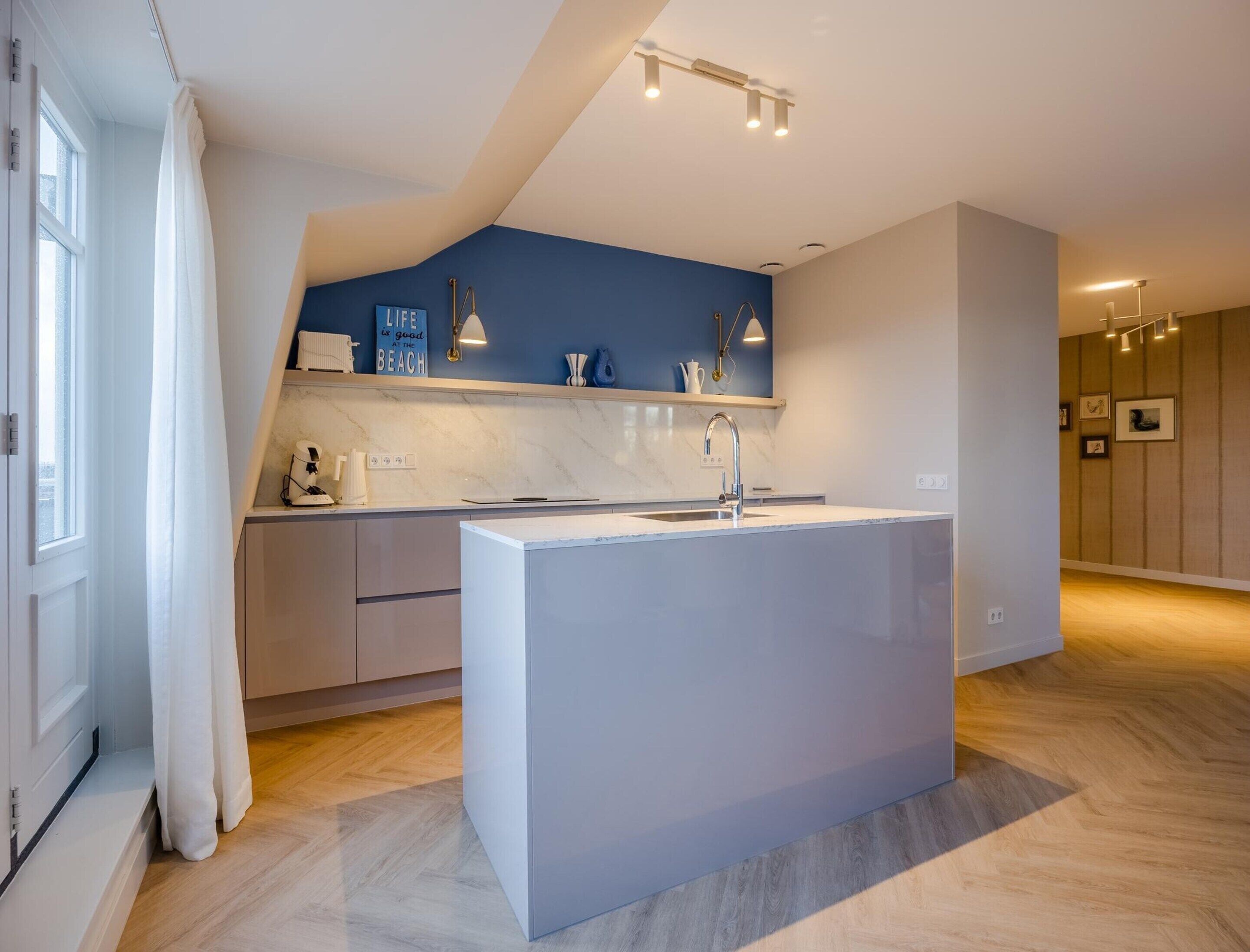 A modern kitchen with a central island, a blue accent wall, and a wooden floor.
