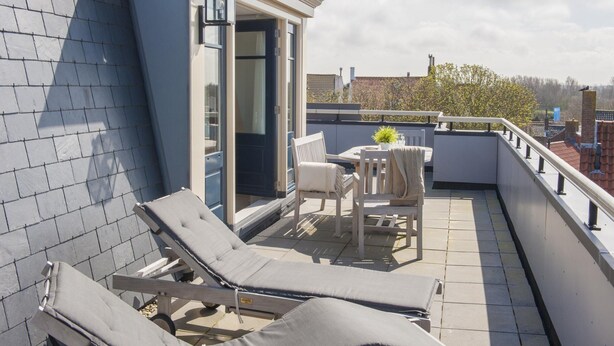 Eine Dachterrasse mit zwei Liegestühlen, einem Tisch mit Topfpflanze und einer Tür zu einem Innenbereich.