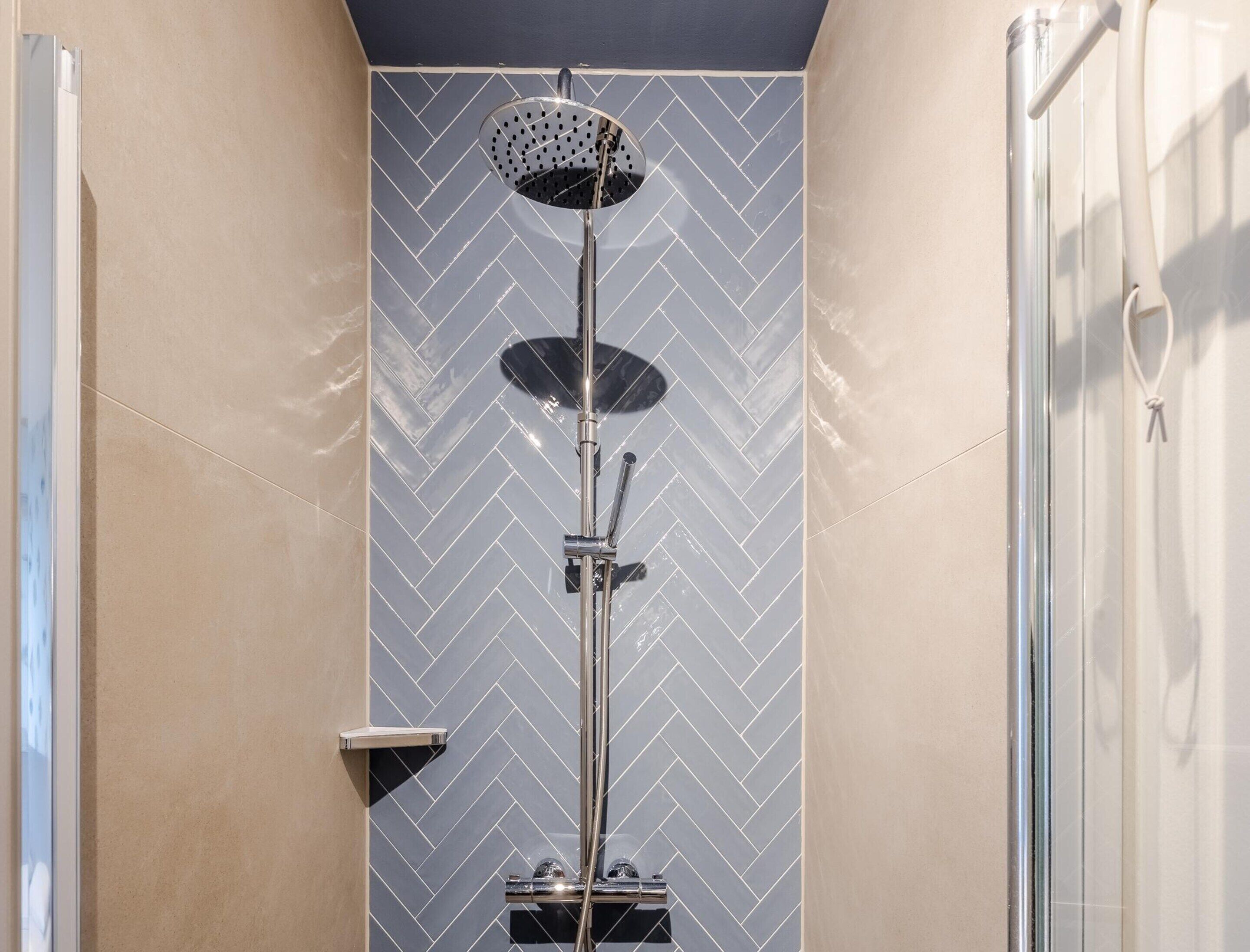 A shower with a herringbone tile pattern and a handheld showerhead.