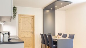 A compact kitchen with a coffee machine, a wooden door, and a dining area with a table and chairs.
