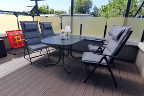 An outdoor patio with a round table and four chairs, a small table with a vase and lamp, and a red decorative item.