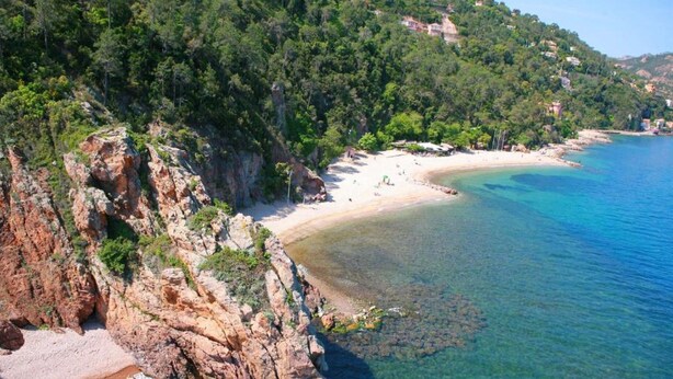 A coastal landscape with a rocky beach, clear blue waters, and a forested hillside. - Luxury Apartment With Large Terrace (Mandelieu-La-Napoule)