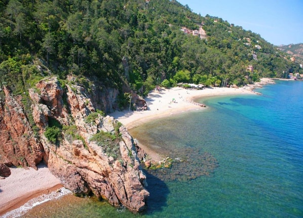 A coastal landscape with a rocky beach, clear blue waters, and a forested hillside. - Luxury Apartment With Large Terrace (Mandelieu-La-Napoule)