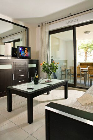 Une chambre d’hôtel moderne dotée d’une table à manger en verre, d’un canapé, d’une télévision et d’un balcon avec un coin repas.