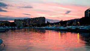 A marina at dusk with boats docked, buildings in the background, and a calm water surface reflecting lights. - Luxury Apartment With Large Terrace (Mandelieu-La-Napoule)