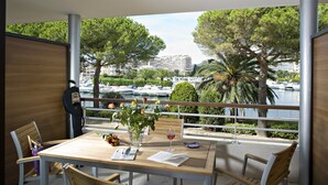 A balcony with a wooden table, chairs, a vase with flowers, a wine glass, and a menu. - Luxury Apartment With Large Terrace (Mandelieu-La-Napoule)