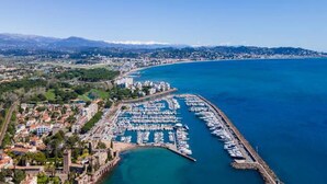 An aerial view of a coastal marina with boats docked, a clear sky, and a cityscape in the background. - Luxury Apartment With Large Terrace (Mandelieu-La-Napoule)