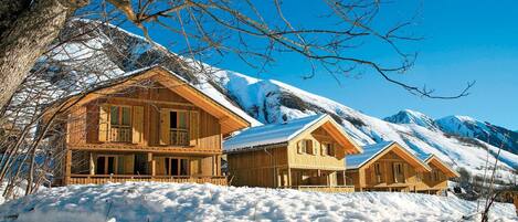 Una cabaña de madera con balcón, rodeada de montañas nevadas.
