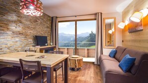 Una habitación con una mesa de comedor de madera, sillas, televisor, sofá y un amplio ventanal con vistas a la montaña.