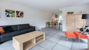 A modern living room with a black sofa, a wooden coffee table, and orange chairs. There is a kitchen area in the background with a dining table and chairs. - Nice House With Dishwasher, Near Amsterdam (Uitgeest)