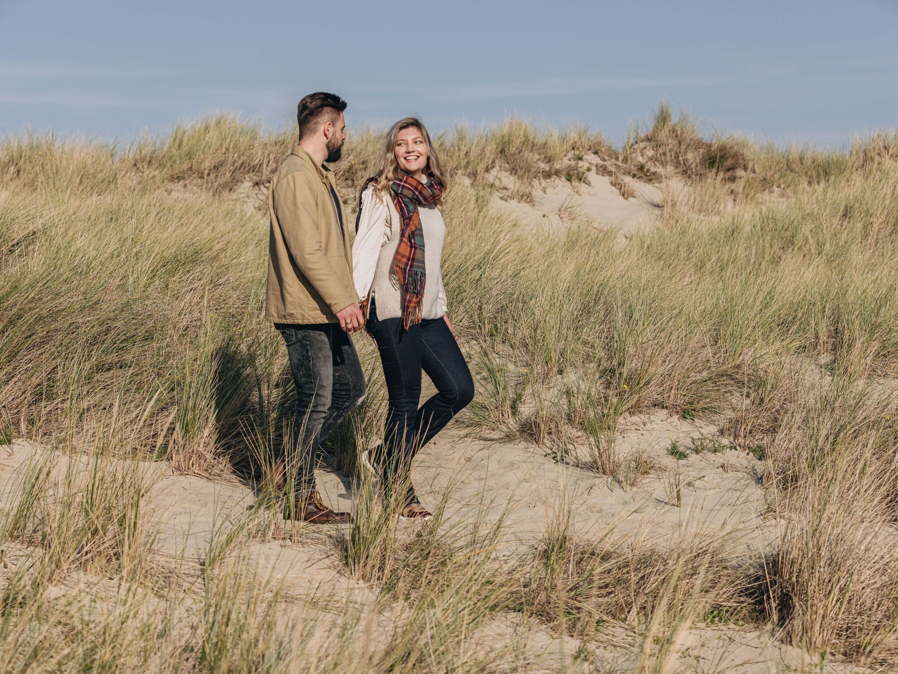 A couple standing in a grassy area with sand dunes in the background.
