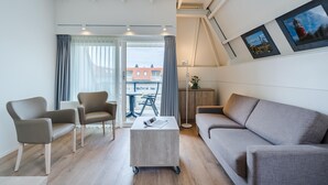 Ein modernes Wohnzimmer mit einem grauen Sofa, zwei Sesseln, einem Couchtisch und Blick auf den Außenbalkon.