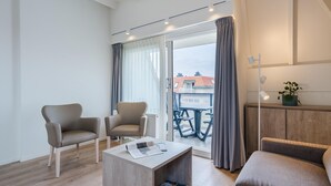 Ein modernes Wohnzimmer mit zwei Sesseln, einem Couchtisch und einer Couch. Eine Glastür verschiebt sich zu einem Außenbereich mit Tisch und Stühlen.