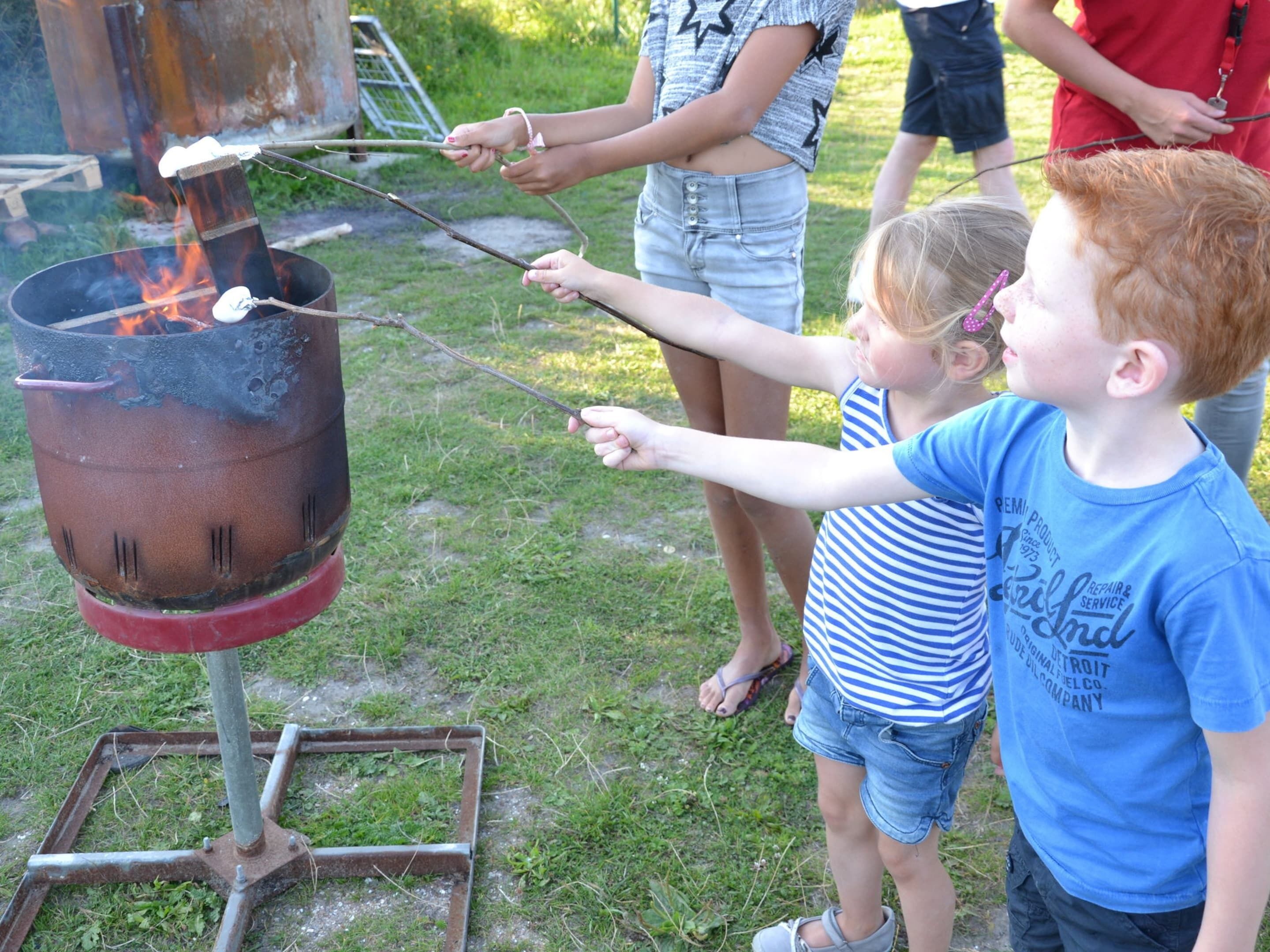 A group of people roasting marshmallows over a metal grill outdoors.