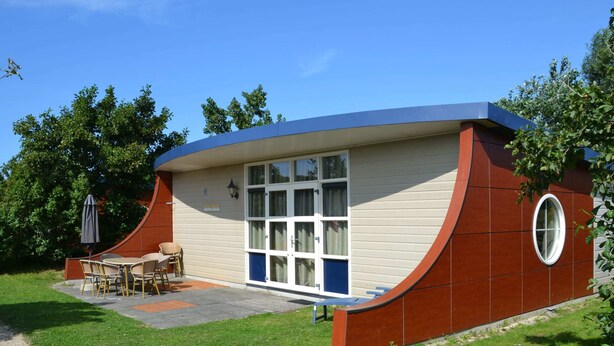 A modern house with a curved roof, a patio with outdoor furniture, and a large window. - Bungalow in Dunes With Nautical Charm ('s-Gravenzande)