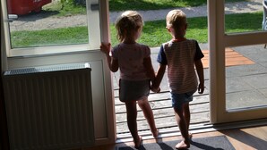 Two children holding hands at a glass door with a view of a red wagon outside. - Bungalow in Dunes With Nautical Charm ('s-Gravenzande)