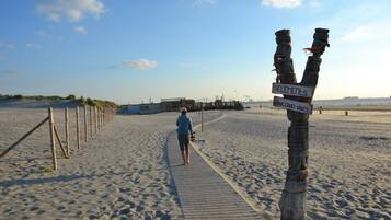 Een zandstrand met een houten looppad, een persoon die loopt en een bord met tekst.