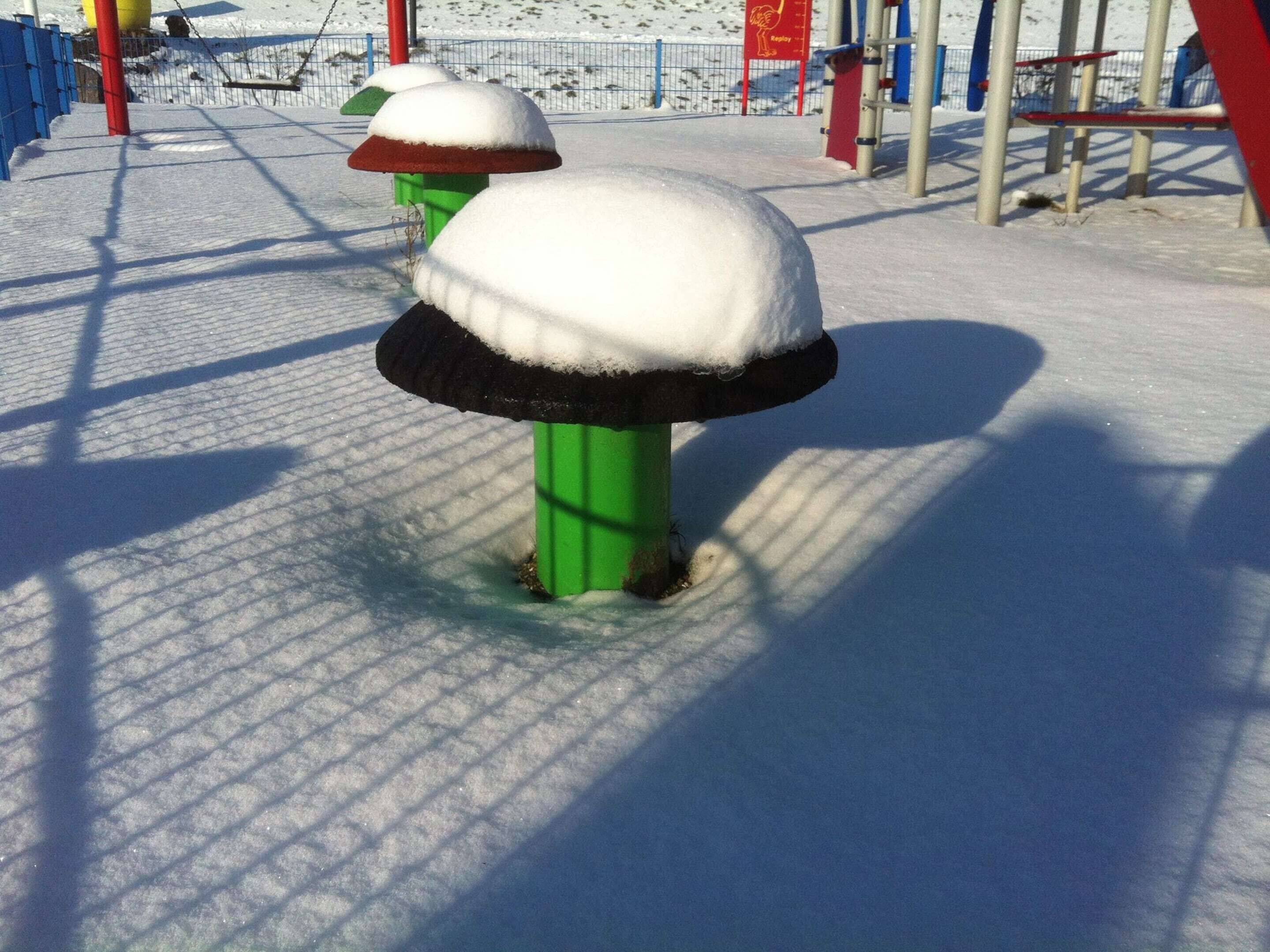 A snow-covered outdoor area with a metal fence and a playground structure.
