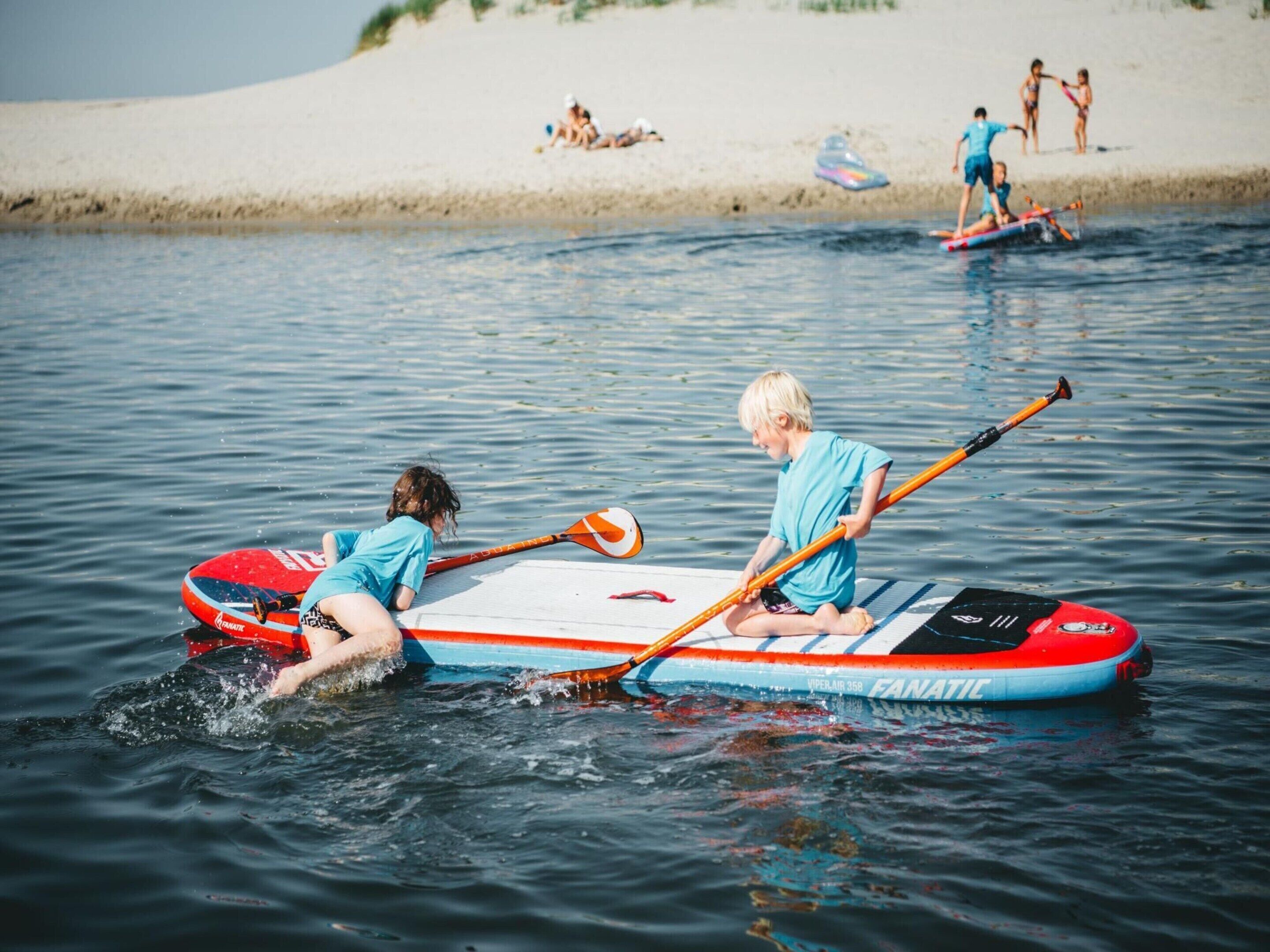 Iemand in een blauw shirt peddelt op een rood-wit paddleboard over kalm water.