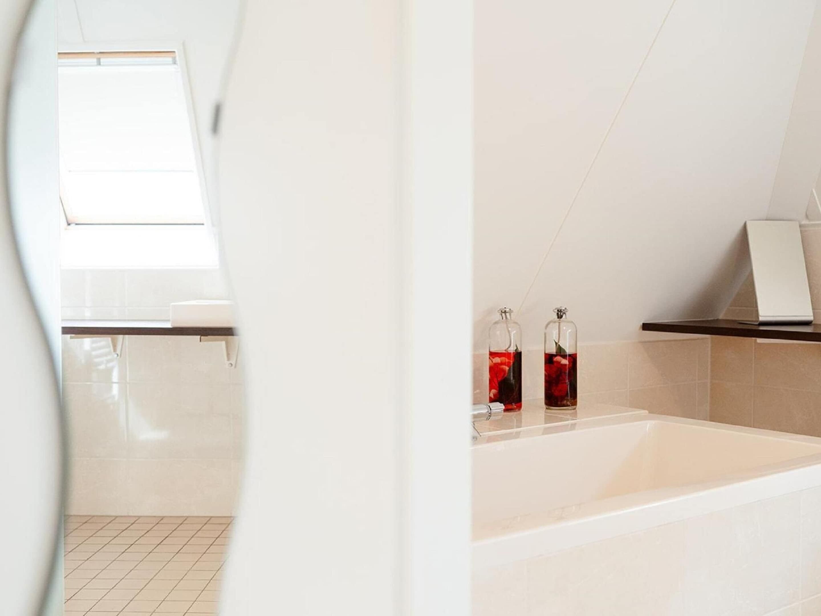 A modern bathroom with a large bathtub, a window, and two glass bottles with red liquid on the side.