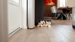 Un intérieur moderne avec un plancher en bois, un coin repas comprenant des chaises et une table, et une cheminée avec des bûches.