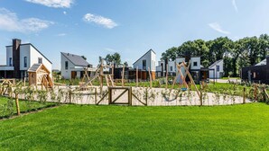 Zona residencial con casas modernas, un parque infantil y césped cuidado.