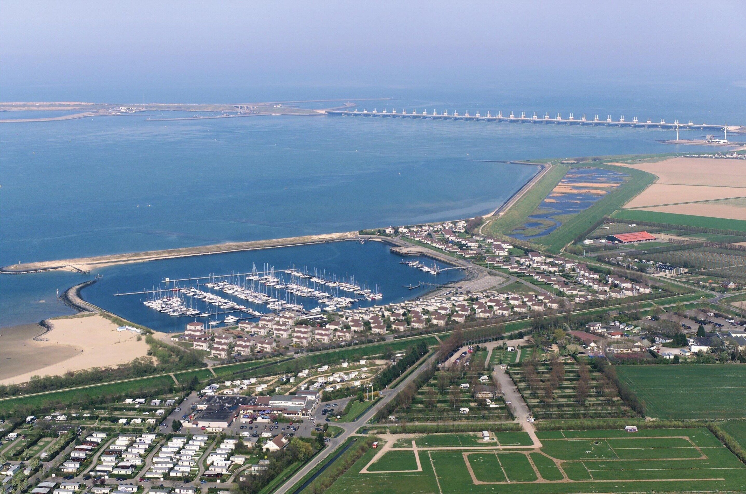 Vue aérienne d’une ville côtière avec un port de plaisance, des zones résidentielles et un pont au loin.