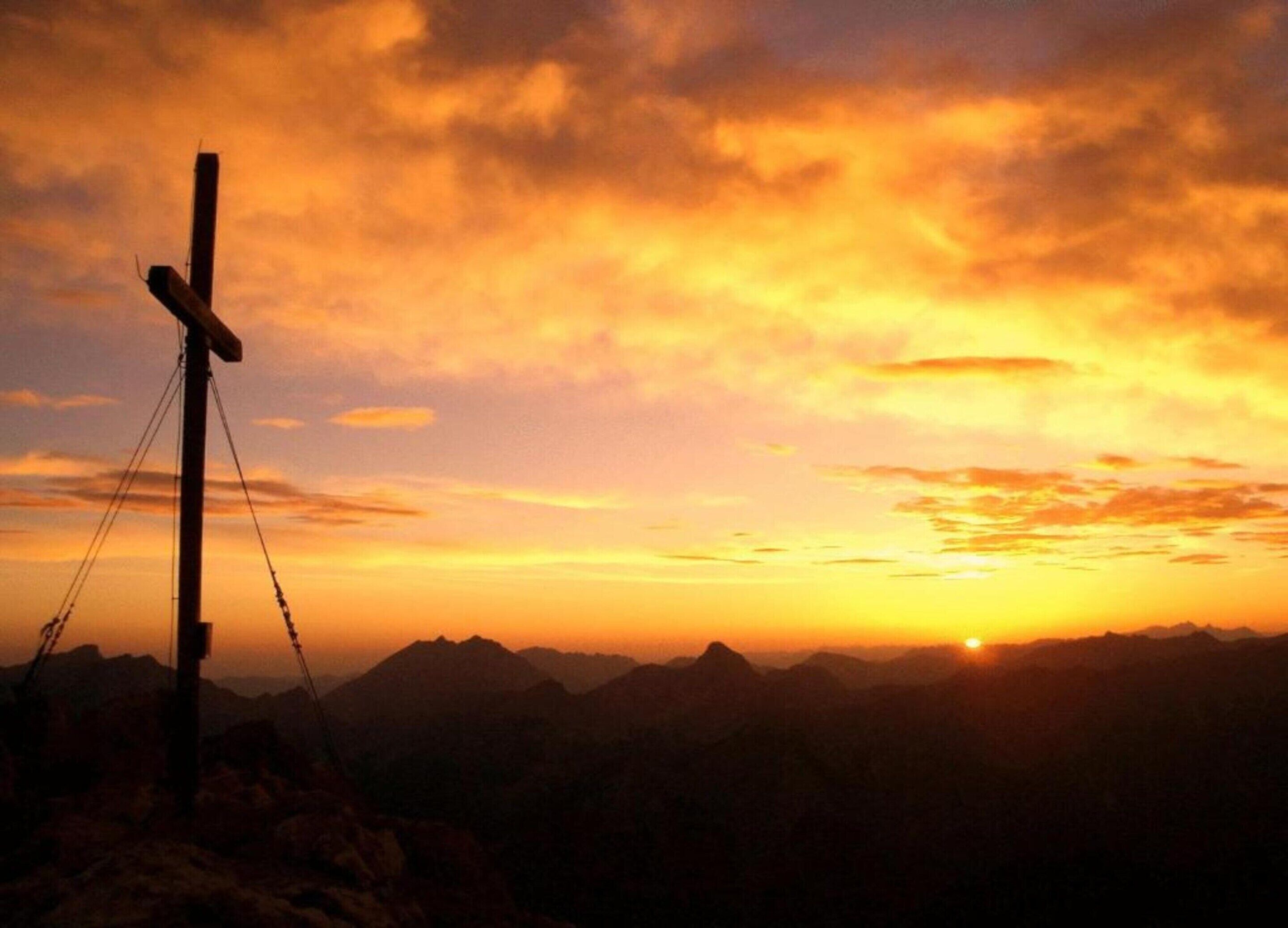 A sunset over a mountainous landscape with a wooden cross structure.
