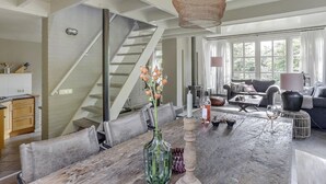 A spacious living area with a large wooden dining table, a staircase, and a cozy seating area with a sofa and armchairs. - Luxury Villa in De Pier With Sauna (Uden)
