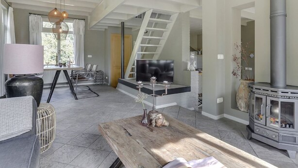 A spacious living room with a high ceiling, a fireplace, a dining area, and a staircase leading to an upper level. - Luxury Villa in De Pier With Sauna (Uden)