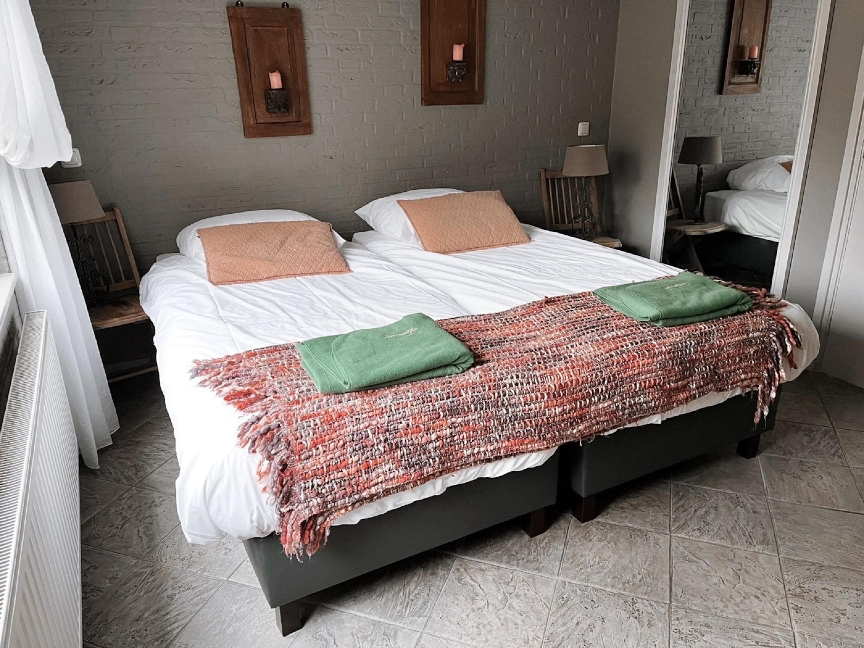 Une chambre à coucher avec un lit, deux tables de chevet, un miroir et une fenêtre avec des rideaux.