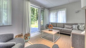 Ein modernes Wohnzimmer mit grauem Sofa, einem Couchtisch und Blick auf einen Garten durch eine Schiebeglastür.