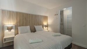 Ein modernes Hotelzimmer mit einem großen Bett, zwei Nachttischlampen, einem Holz-Kopfteil, einer Dusche und einem begehbaren Kleiderschrank.