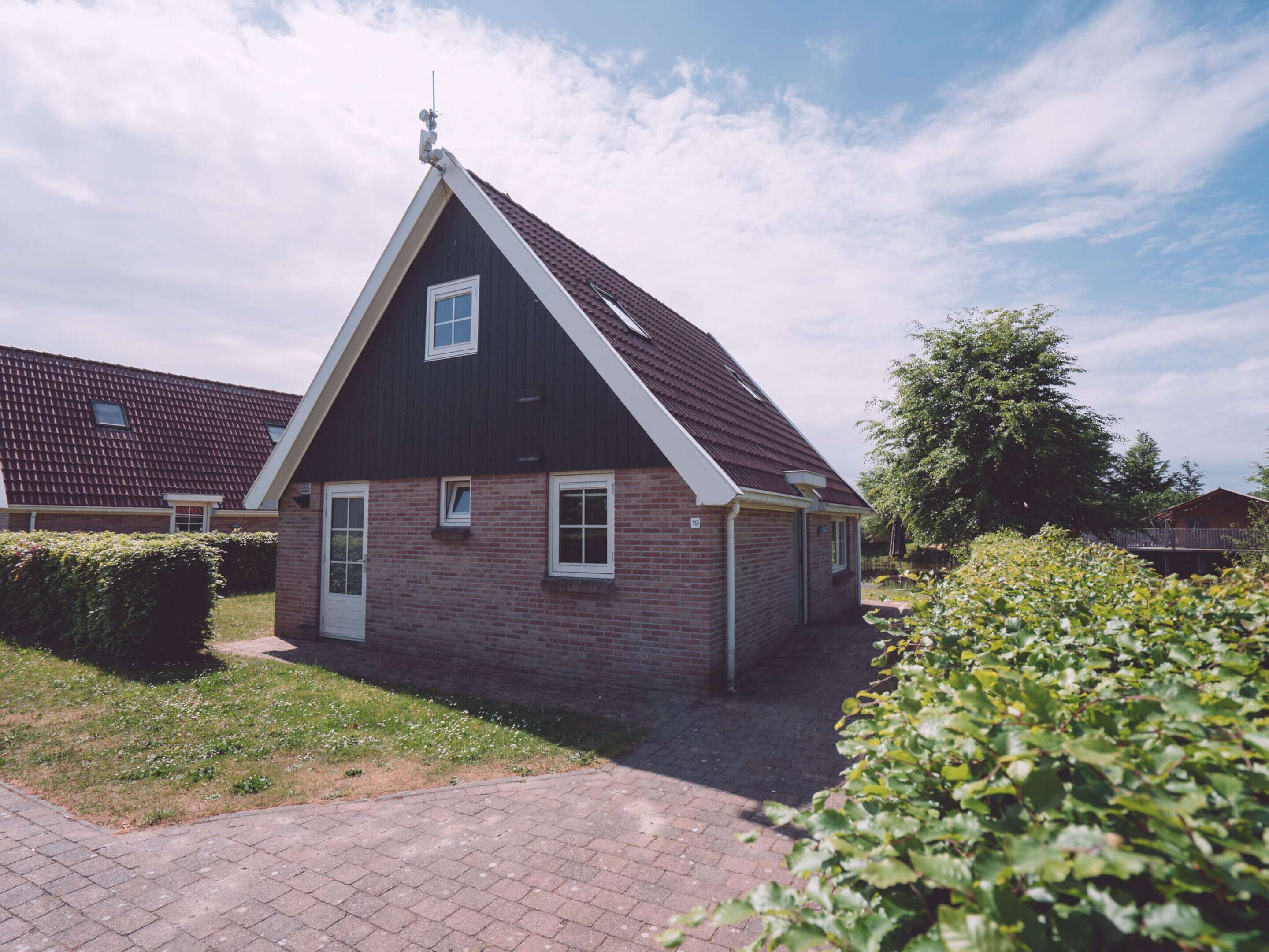 Ein eingeschossiges Haus mit dunklem Dach und Backsteinwänden, einer kleinen Veranda und einem gepflasterten Auffahrt.