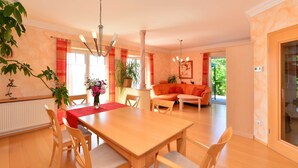 A spacious dining area with a wooden table and chairs, a chandelier, and a large window with curtains.