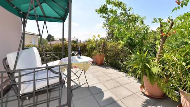 A patio with a table, chairs, and a green canopy. There are potted plants and a view of a garden.