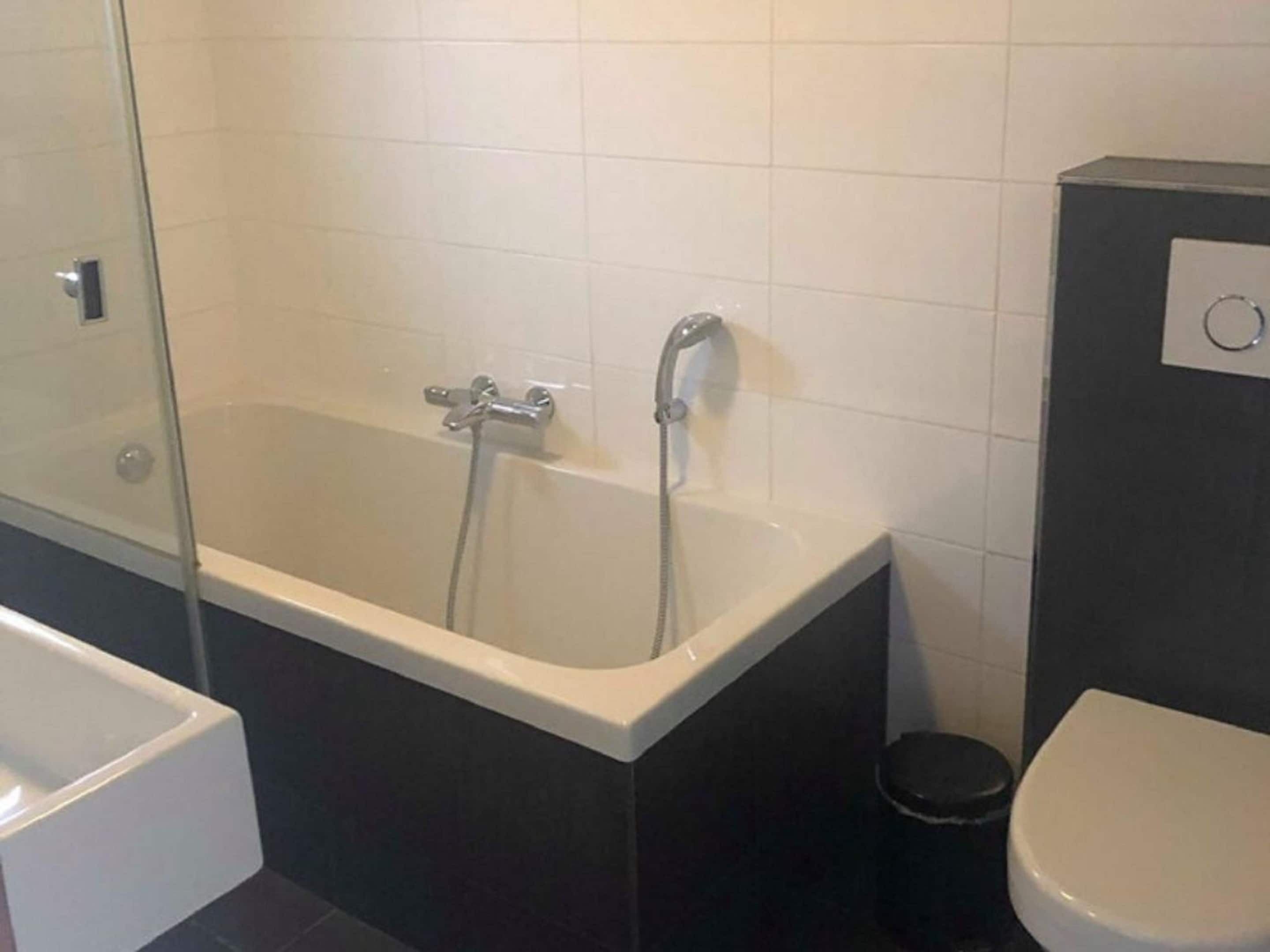 A modern bathroom with a bathtub, a toilet, and a glass shower enclosure.